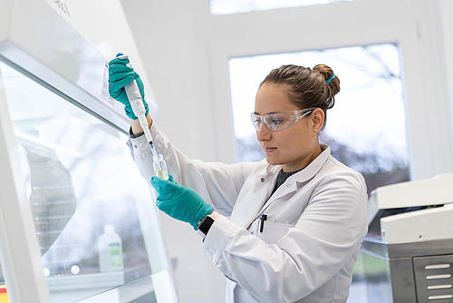 Frau im Laborkittel mit Schutzbrille und Handschuhen führt einen Labortest durch